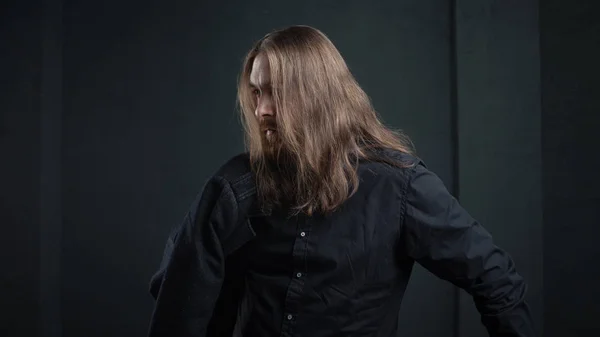 Portrait of man with long hair and beard in black clothes on dark background — Stock Photo, Image