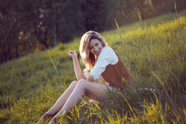 Mutlu kadın beyaz gömlekli doğada bir piknik keyfi. Çim, dinlenme, rahatlama üzerinde oturan kız