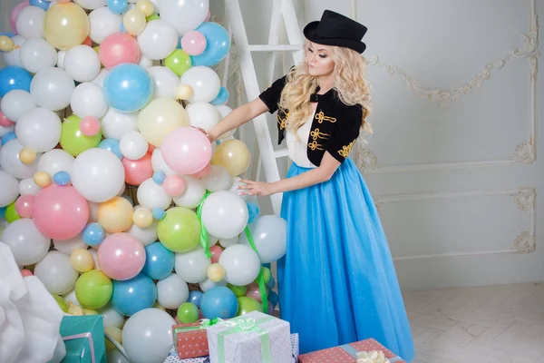 Een mooie blonde in een carnaval kostuum siert de boom van ballonnen. Charmante jongedame in een bochtige blauwe rok. — Stockfoto