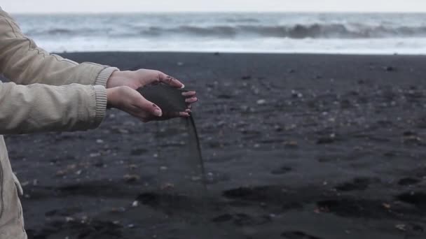 Island, svart sand. Kvinnliga händer på nära håll, för att hälla sand genom fingrarna — Stockvideo