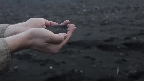 Island, černým pískem. Pánské ruce blízko, hrst sopečného písku — Stock video