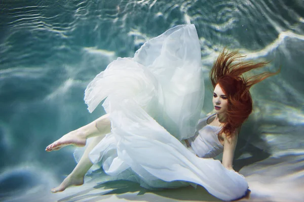 Sualtı kız. Su altında yüzme beyaz bir elbise, güzel kızıl saçlı kadın.