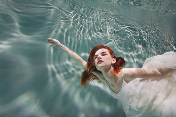 Rapariga subaquática. Mulher ruiva bonita em um vestido branco, nadando sob a água . — Fotografia de Stock