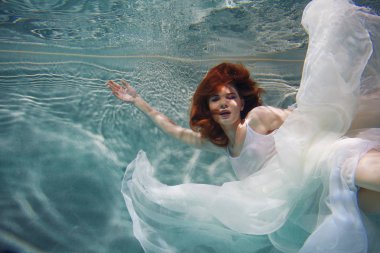 Sualtı kız. Su altında yüzme beyaz bir elbise, güzel kızıl saçlı kadın.