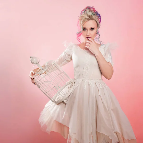 Menina na moda em vestido branco. Coloração de cabelo criativo. Penteado multicolorido. Conceito com uma gaiola de pássaro vazia . — Fotografia de Stock