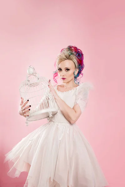 Menina elegante em vestido branco. Coloração de cabelo criativo. Penteado multicolorido. Conceito com uma gaiola de pássaro vazia . — Fotografia de Stock