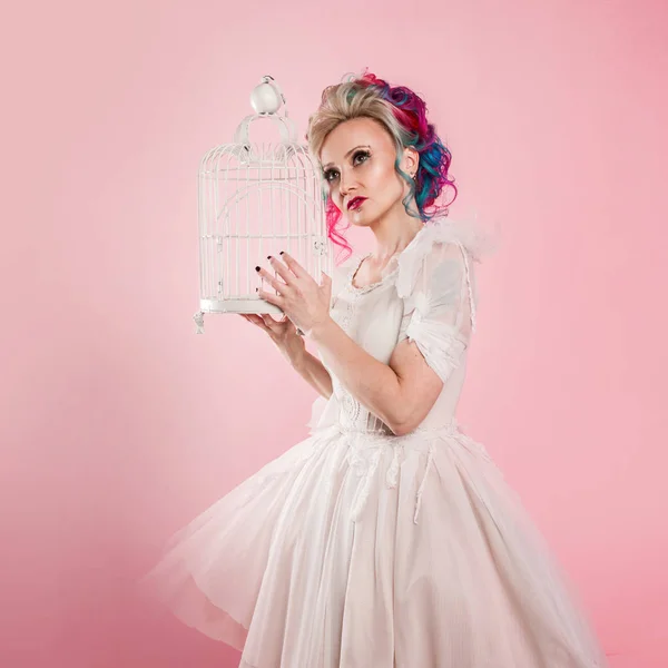 Menina elegante em vestido branco. Coloração de cabelo criativo. Penteado multicolorido. Conceito com uma gaiola de pássaro vazia . — Fotografia de Stock