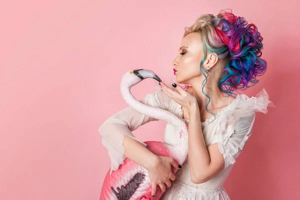 Donna elegante e bella con i capelli colorati. Abbracciare una figura fenicottero rosa . — Foto Stock