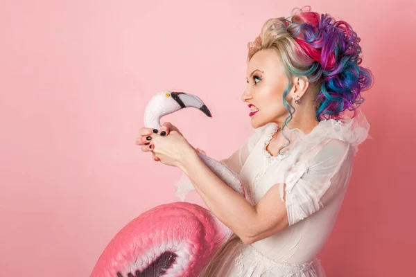 Femme élégante et belle avec des cheveux colorés. Étrange une figurine rose Flamingo . — Photo