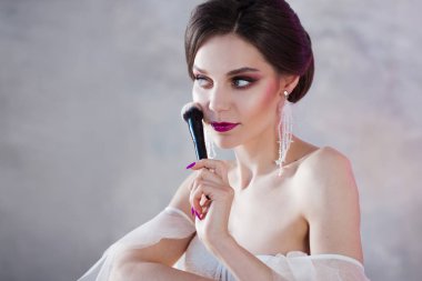 Güzel genç kadın kendini bir makyaj yapıyor. Yüzünde toz el uygulamak için fırça kızla