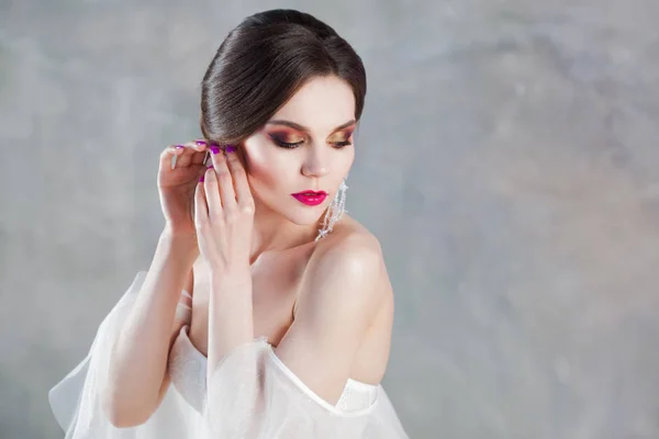 Belle et élégante mariée en robe de mariée en studio met des boucles d'oreilles — Photo