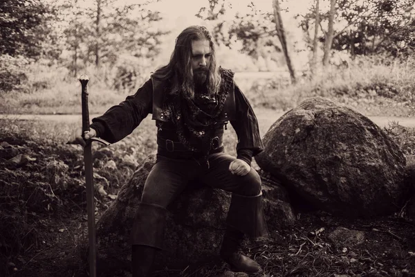 Knight in the forest. Guy in medieval costume with sword. effect of toning — Stock Photo, Image