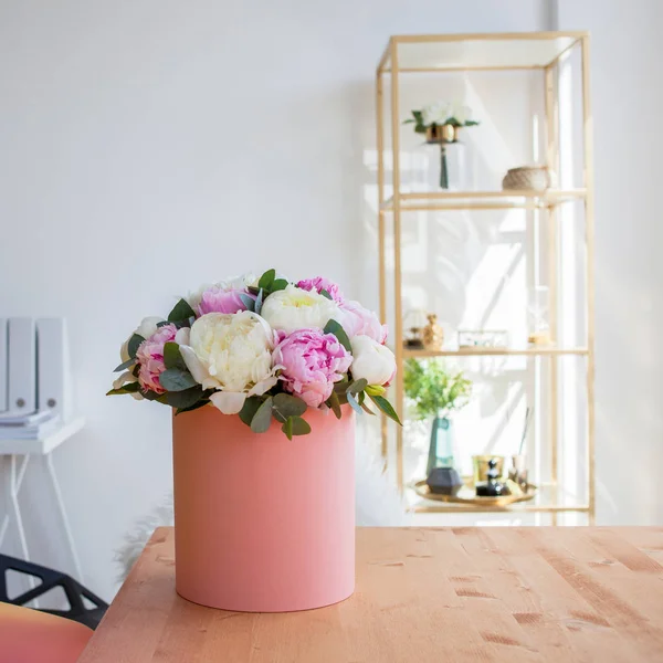 Доставка квітів в офіс. Робочий простір, стіл з блокнотами та журналами. Розкішний букет з півоній в рожевій коробці . — стокове фото