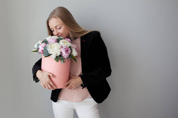 Charming blonde woman with flowers in a hat box. Bouquet of peonies.