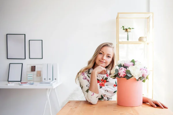 Happy blonde woman in a modern office with flowers in a hat box. Bouquet of peonies. — Stock Photo, Image