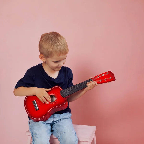 O rapazinho está a aprender a tocar numa guitarra pequena. Estudar música. Ukulele — Fotografia de Stock