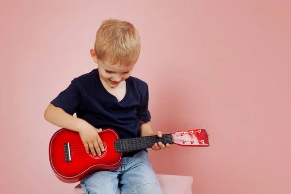 O rapazinho está a aprender a tocar numa guitarra pequena. Estudar música. Ukulele — Fotografia de Stock