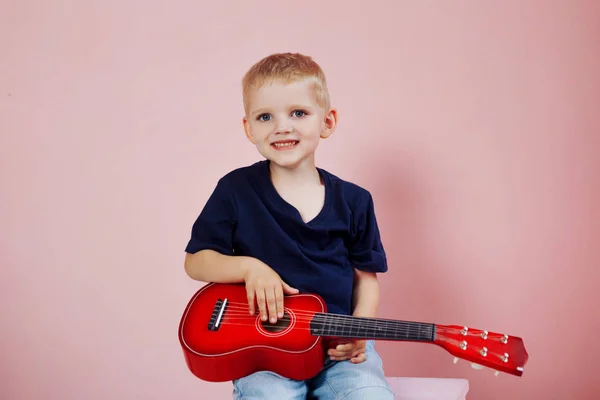 El niño está aprendiendo a tocar en una pequeña guitarra. Estudia música. Ukulele — Foto de Stock