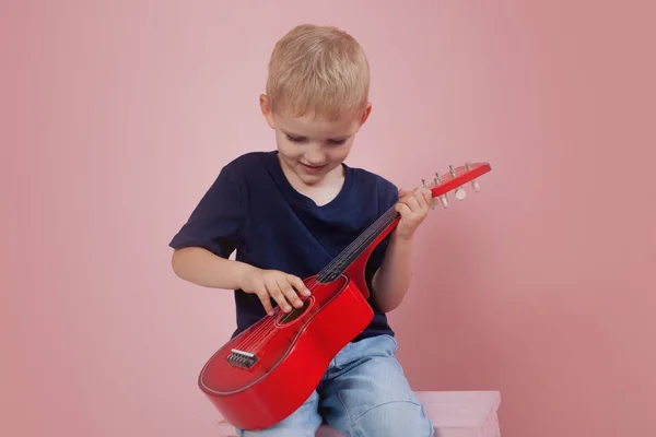 El niño está aprendiendo a tocar en una pequeña guitarra. Estudia música. Ukulele — Foto de Stock