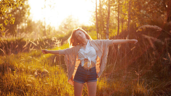 Happy young woman enjoying a wonderful evening. Warm weather, summer, field. Standing with embraced arms