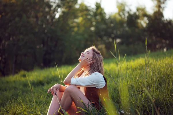 Lycklig kvinna i vit skjorta njuter av en picknick i naturen. Flicka sitter på gräset, vila, avkoppling — Stockfoto