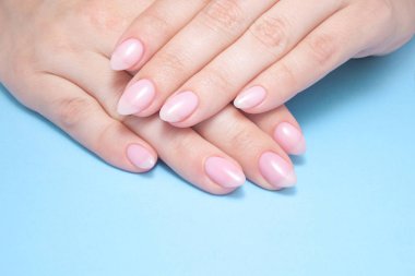 Kadınların elleri ile mükemmel çıplak manikür. Tırnak cilası doğal soluk pembe gölge var. Mavi arka plan