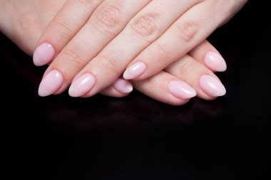 Kadınların elleri ile mükemmel çıplak manikür. Tırnak cilası doğal soluk pembe gölge var. Siyah arka plan