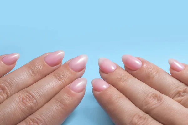 Kvinnors händer med perfekt naken manikyr. Nagellack är en naturlig blek rosa nyans. Blå bakgrund — Stockfoto