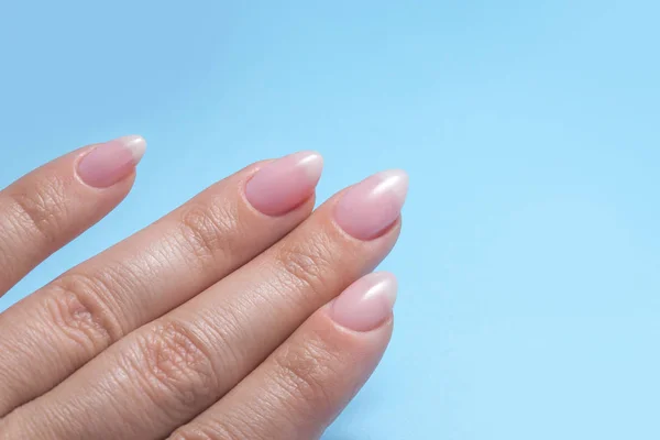 Les mains des femmes avec manucure parfaite Nu. vernis à ongles est une teinte rose pâle naturel. Fond bleu — Photo