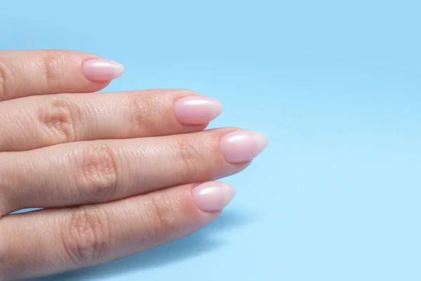 Mãos de mulher com manicure Nude perfeito. O prego polonês é uma sombra rosa pálida natural. Fundo azul — Fotografia de Stock