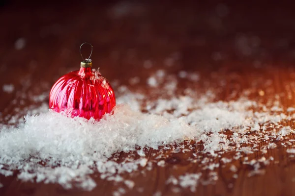 Kırmızı cam top. Noel oyuncak. Kar yığınının içinde Ahşap dokulu arka plan, rustik tarzı