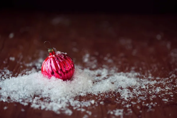 Red glass ball. Christmas toy. In a pile of snow, wood textured background, rustic style — Stock Photo, Image
