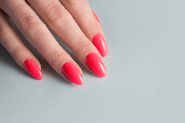 Mãos de mulher com manicure vermelho perfeito. Unha cor de coral vermelho polonês. fundo azul — Fotografia de Stock