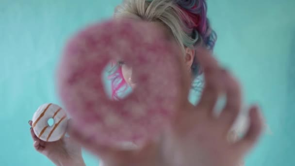 Забавная стильная женщина с цветными волосами, играющая с пончиками — стоковое видео
