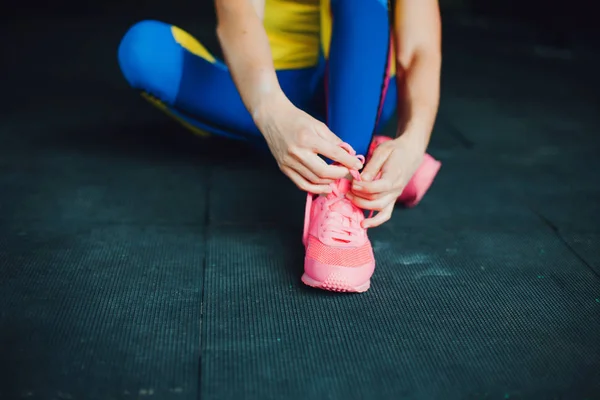 Chica en el club de fitness. Joven atleta sentada en el suelo y atada los cordones de sus zapatos — Foto de Stock
