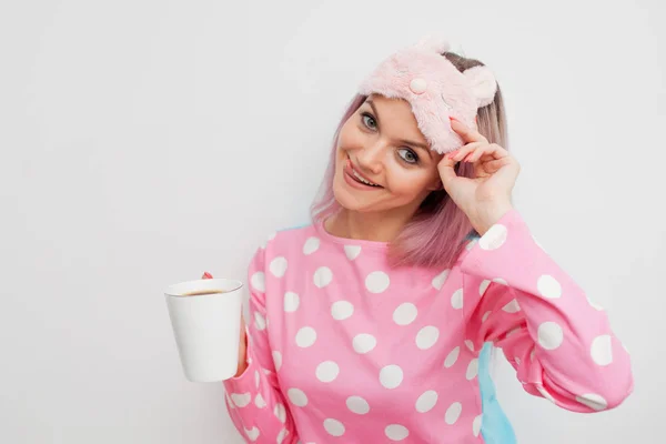 Счастливая девушка пьет утренний кофе. Красивая девушка в розовой пижаме и маске для сна — стоковое фото