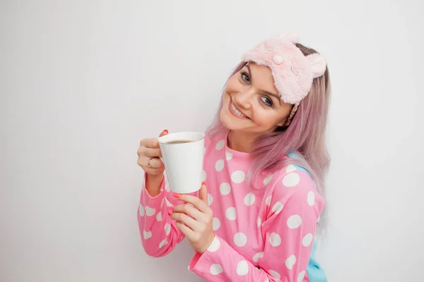 Boldog fiatal nő reggel kávét iszik. Gyönyörű lány rózsaszín pizsama és sleepmask — Stock Fotó