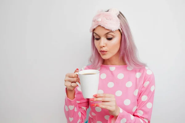 Chica atractiva en pijama rosa y máscara de dormir disfrutando de su café de la mañana —  Fotos de Stock