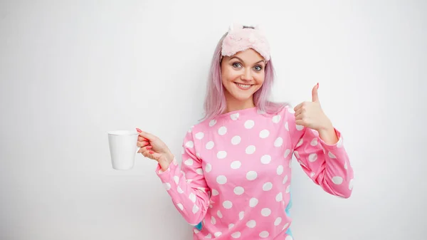 Доброе утро. Улыбающаяся молодая женщина показывает большой палец. Девушка в розовой пижаме и маске для сна — стоковое фото