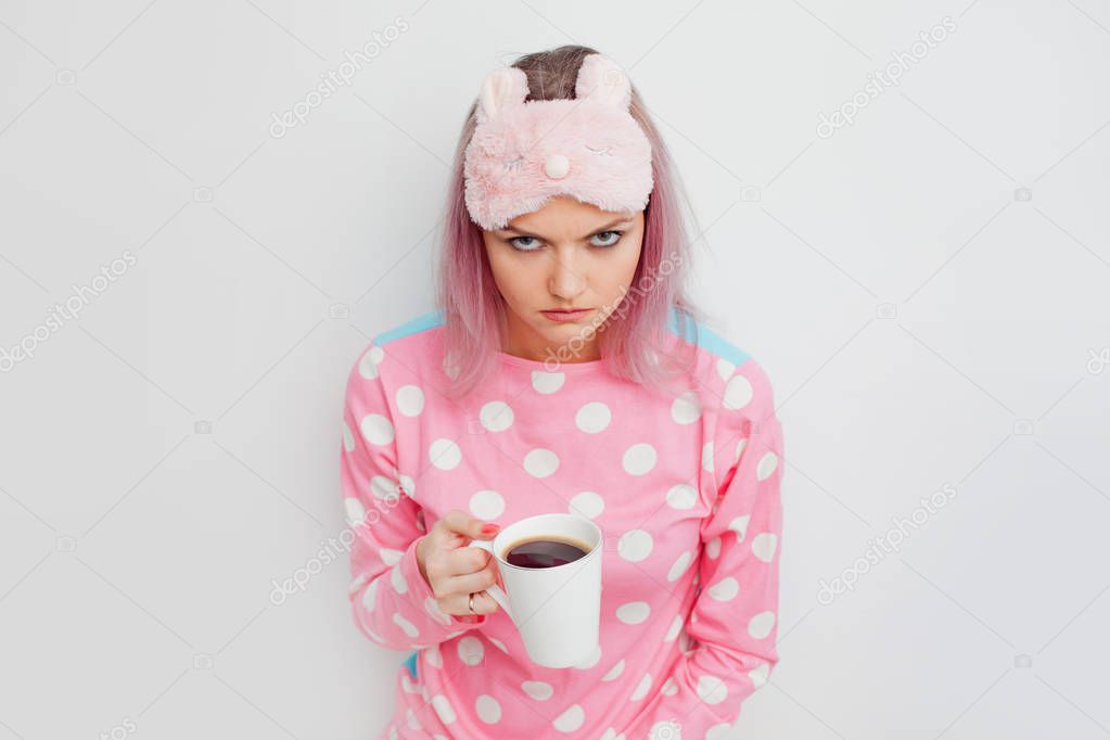 Unhappy girl slept badly. Portrait of grumpy woman in pink pyjamas.