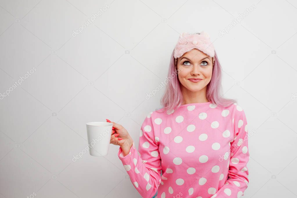 Happy young woman drink morning coffee. Beautiful girl in pink pajamas and sleepmask
