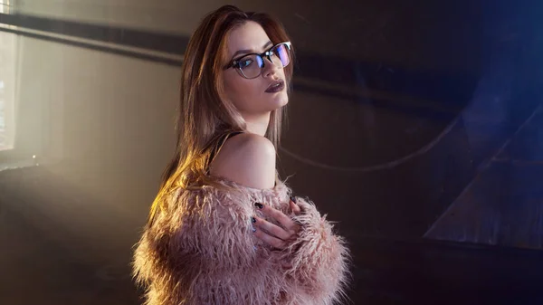 Joven mujer seductora, retrato en la oscuridad. Chica con elegante abrigo de piel rosa y gafas . —  Fotos de Stock