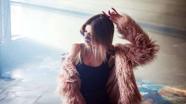 Модная девушка танцует в пушистом розовом пальто
