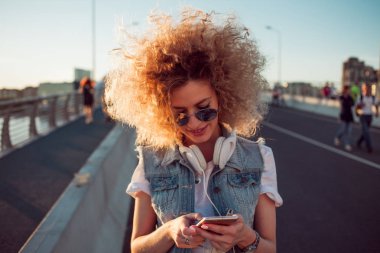 Sokaktaki mutlu genç kız. Güzel sarışın kulaklıklarla kullanmak belgili tanımlık smartphone.