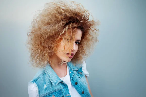 Jovem mulher atraente com cabelo muito exuberante. Retrato de uma menina bonita em colete de ganga — Fotografia de Stock