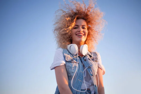 Trendy girl with large headphones on sky background, free space on the right. — Stock Photo, Image