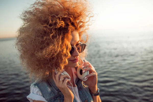 Fille à la mode avec de grands écouteurs et des lunettes de soleil sur une promenade en ville, gros plan — Photo