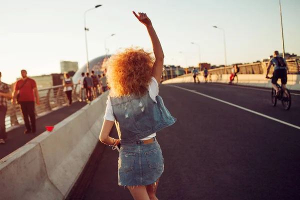 Walking on the street, trendy young woman with lush hair go ahead. Back view. — Stock Photo, Image