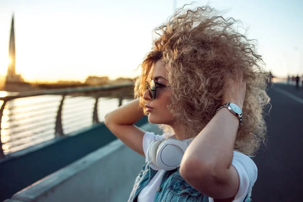 Trendy girl with large headphones and sunglasses on a city walk, young woman portrait in profile — Stock Photo, Image