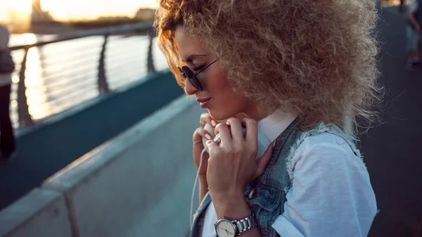 Trendy girl with large headphones and sunglasses on a city walk, young woman portrait in profile